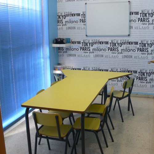 Interior de aula con pared empapelada con nombres de países y mesa grande amarilla en el centro