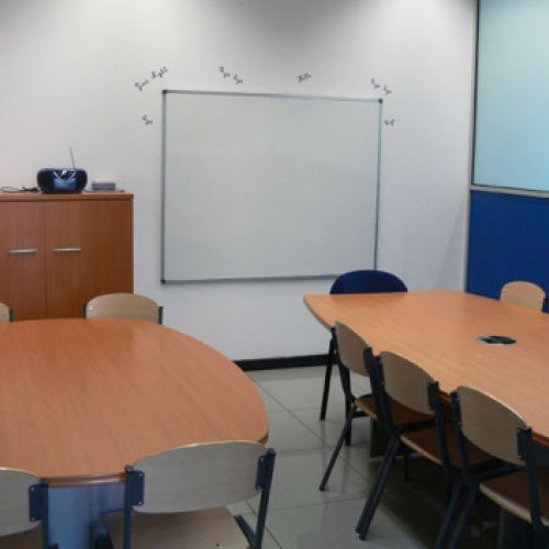 Interior d´aula amb dues taules grans i cadires als costats