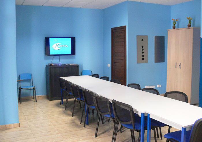Interior de aula con mesa larga en el centro, paredes de color azul y pantalla digital en pared de fondo