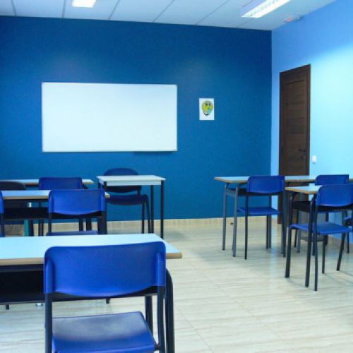 Interior d'aula amb taules, cadires i parets de color blau i pissarra blanca a paret de fons