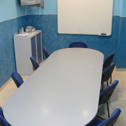 Interior d'aula amb parets de color blau i taula gran ovalada al centre