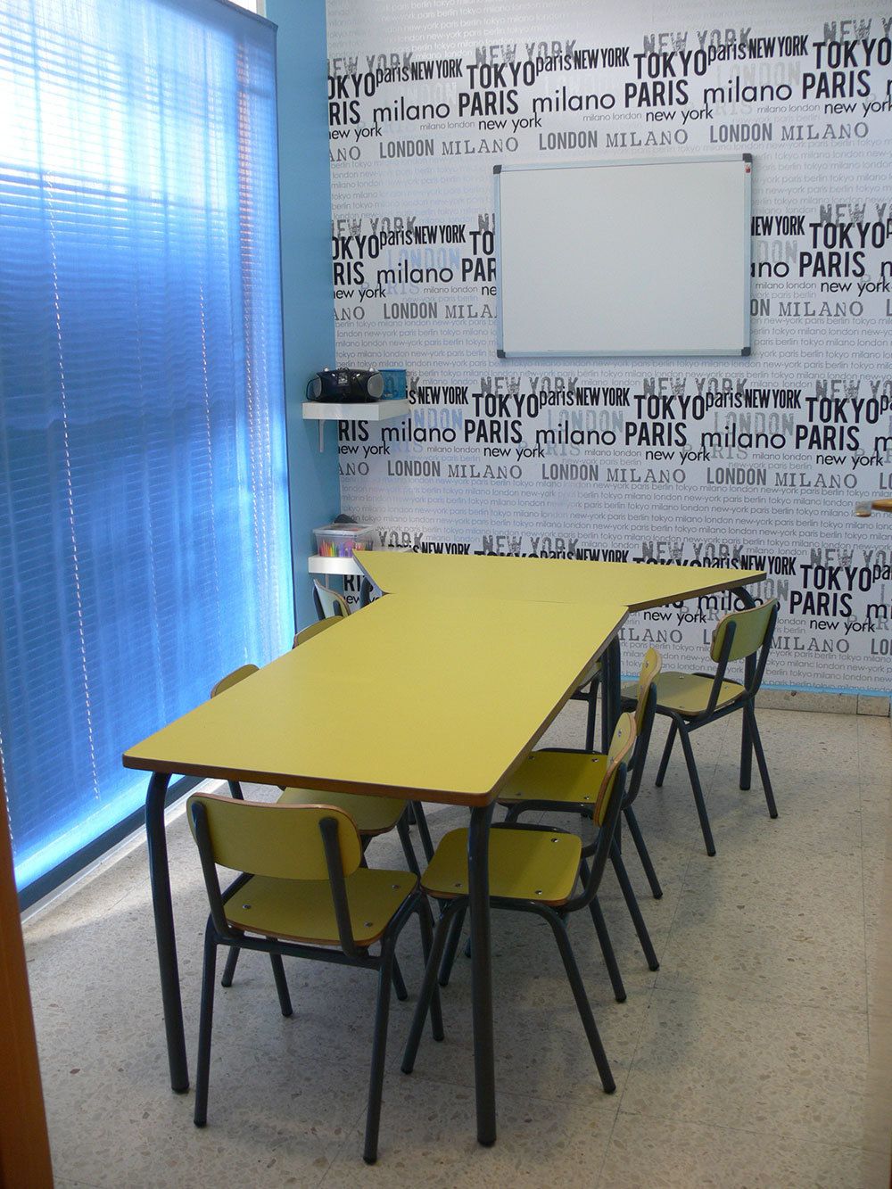 Interior de aula con pared empapelada con nombres de países y mesa grande amarilla en el centro