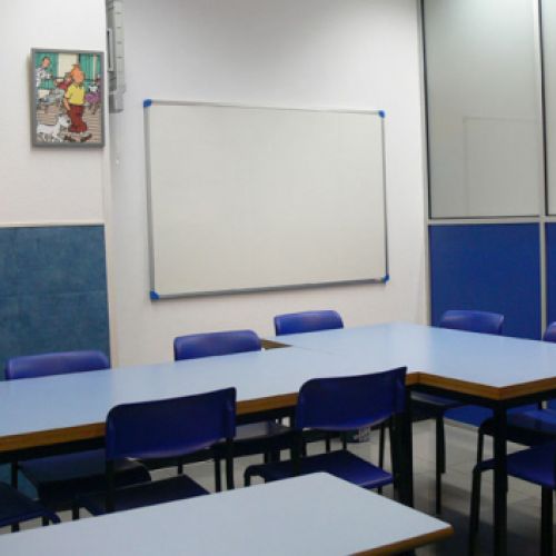 Interior de aula con mesas en L, sillas azules a los lados y cuadros de Tintín en la pared
