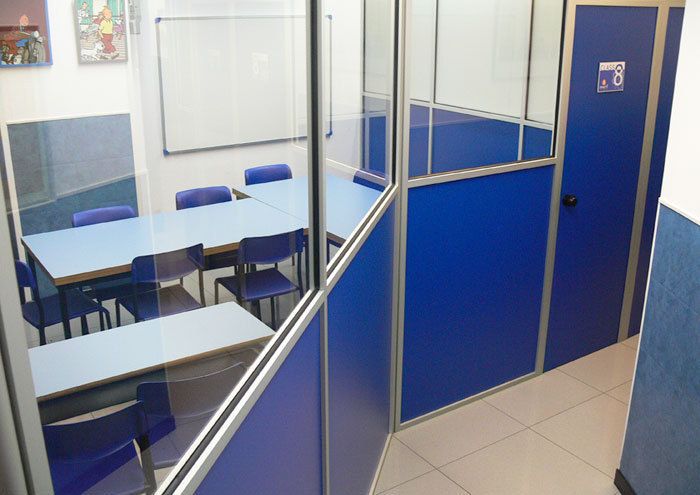 Vista exterior de aula desde pasillo con carpintería y puerta de color azul