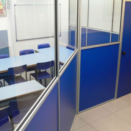 Vista exterior de aula desde pasillo con carpintería y puerta de color azul