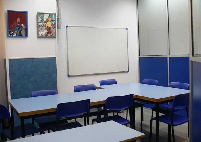 Interior de aula con mesas en L, sillas azules a los lados y cuadros de Tintín en la pared