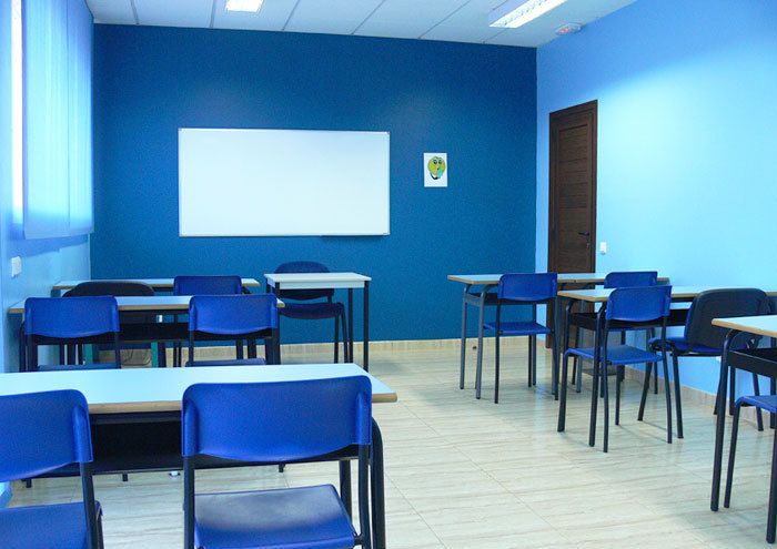 Interior de aula con mesas, sillas y paredes de color azul y pizarra blanca en pared de fondo