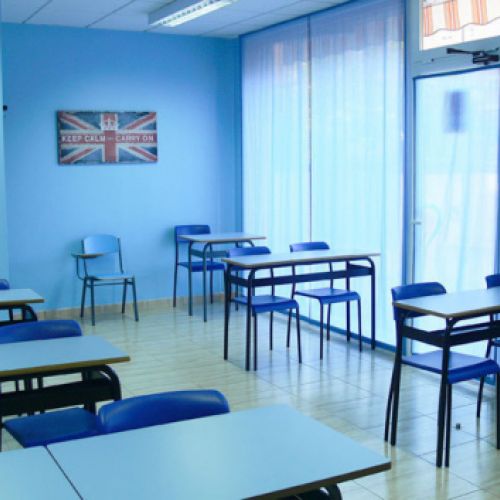 Interior de aula con mesas, sillas y paredes de color azul y cuadro con bandera inglesa en pared de fondo