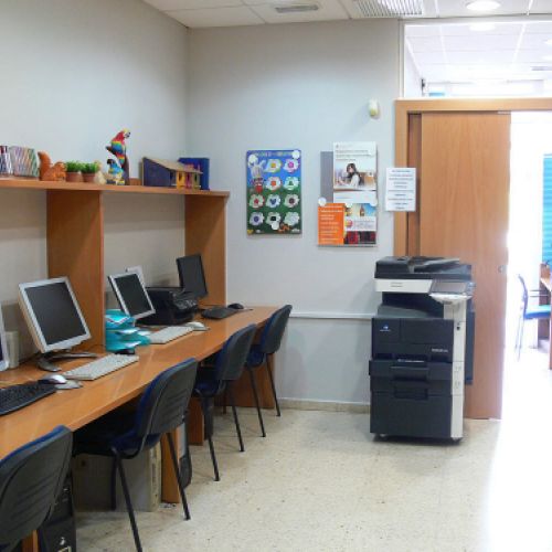 Interior de aula con mesas juntas y ordenadores en un lateral