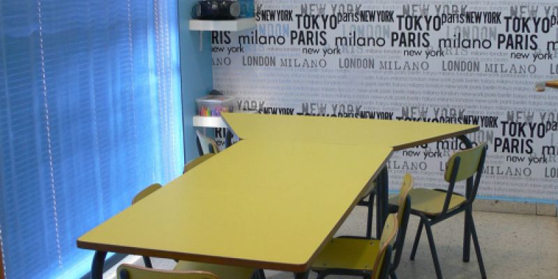 Interior d'aula amb paret empaperada amb noms de països i taula gran groga al centre